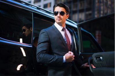 A chauffeur in a suit and tie is getting out of a limousine.