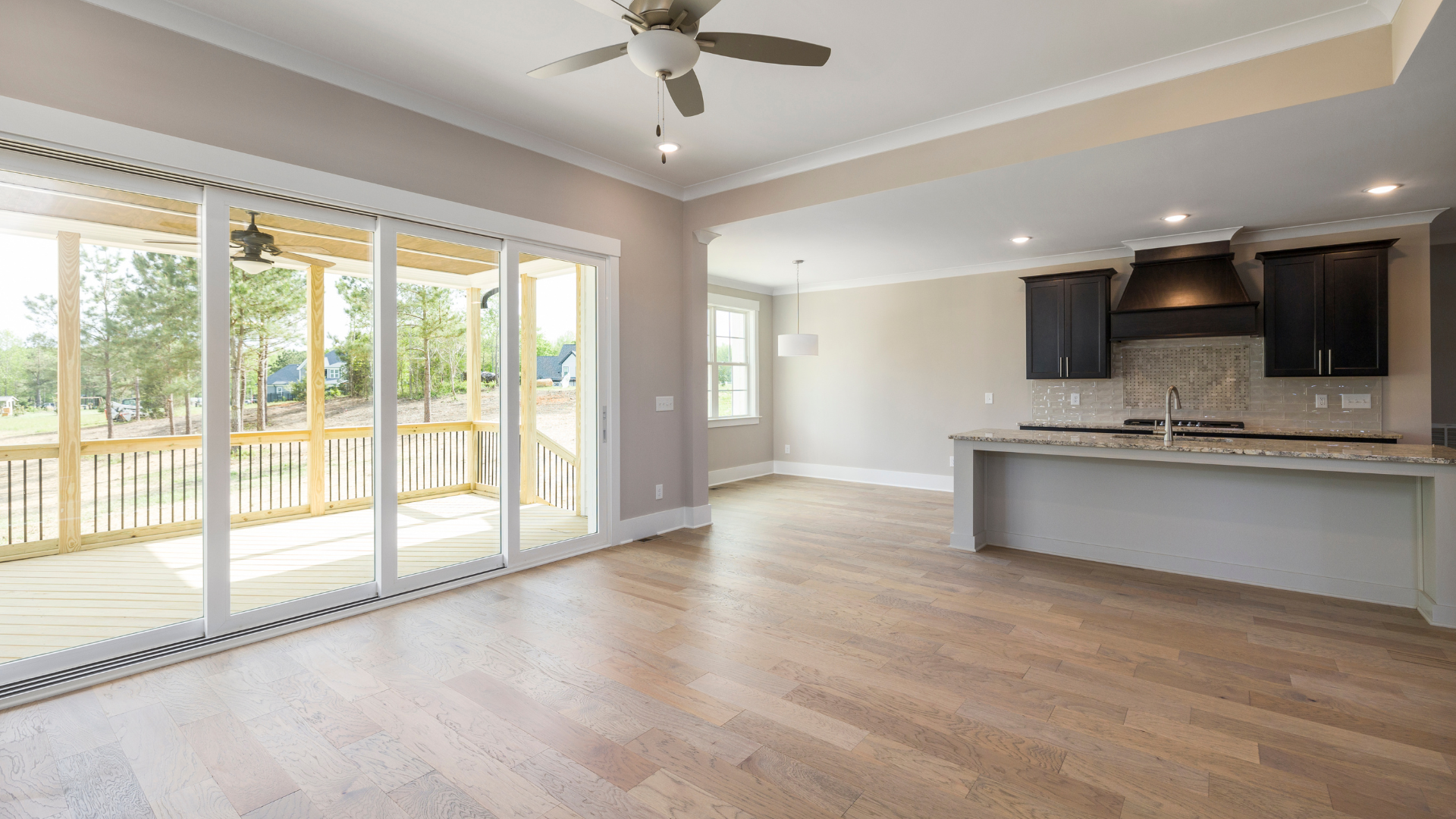 Open-concept living space with wood floors, sliding glass doors to a porch, and a kitchen with dark cabinets.