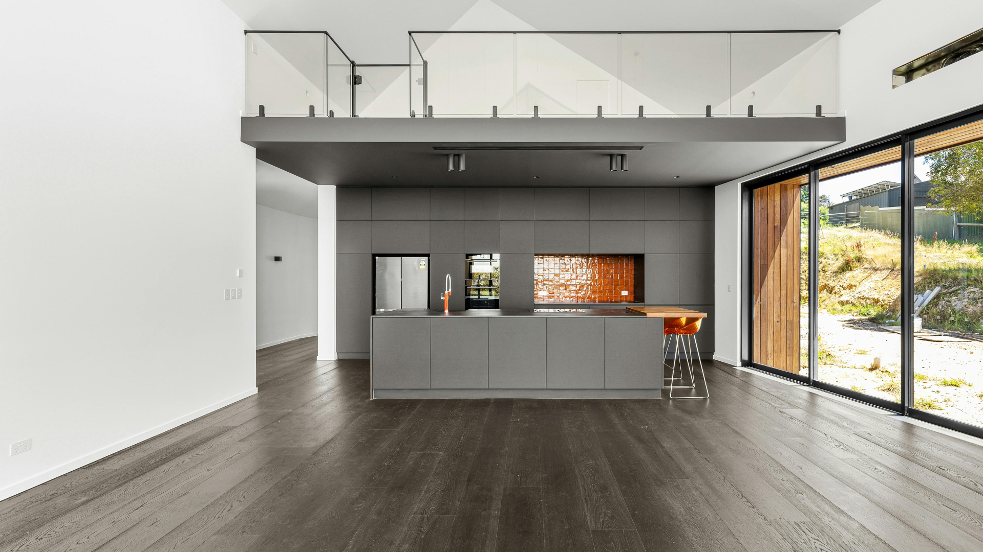 Modern interior: gray kitchen island, loft, dark wood floor, large window, view of nature.