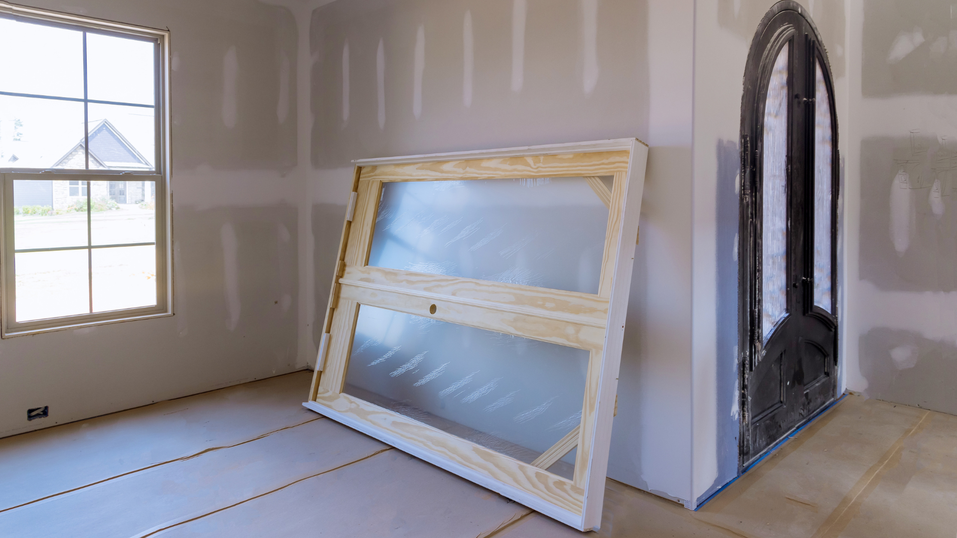 Interior room under construction with a window, drywall, a wooden-framed window, and an arched doorway.