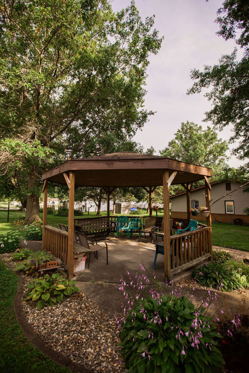 A gazebo with chairs and a table in a garden surrounded by trees.