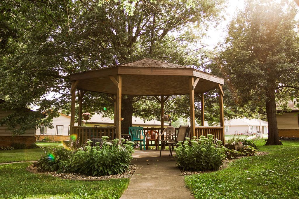 A gazebo with a table and chairs in a park surrounded by trees.