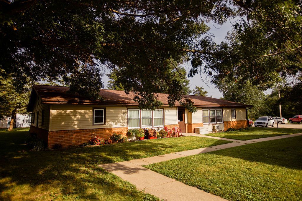 A house with a walkway leading to it is surrounded by trees and grass.