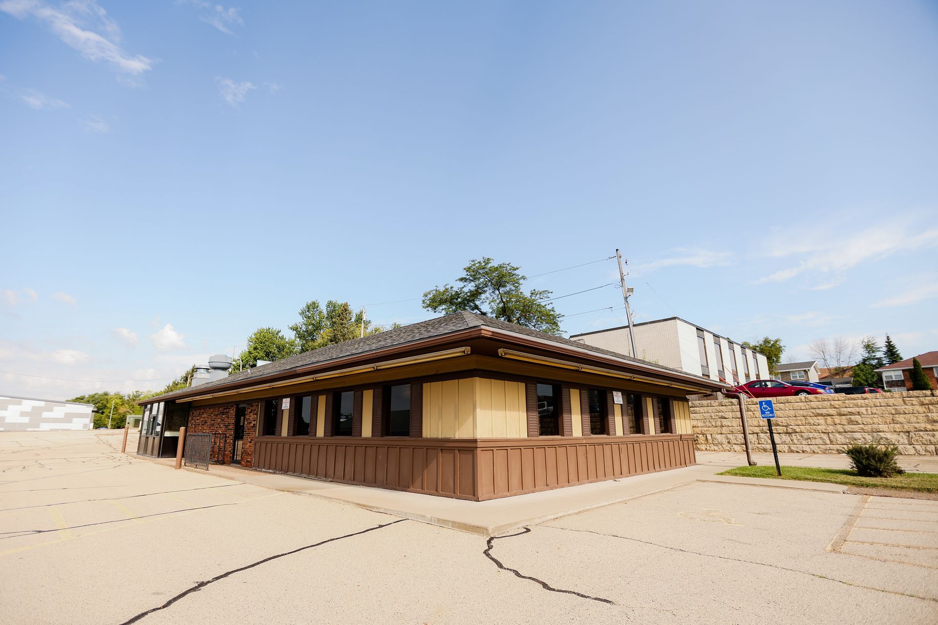 A small building with a lot of windows is sitting in the middle of a parking lot.