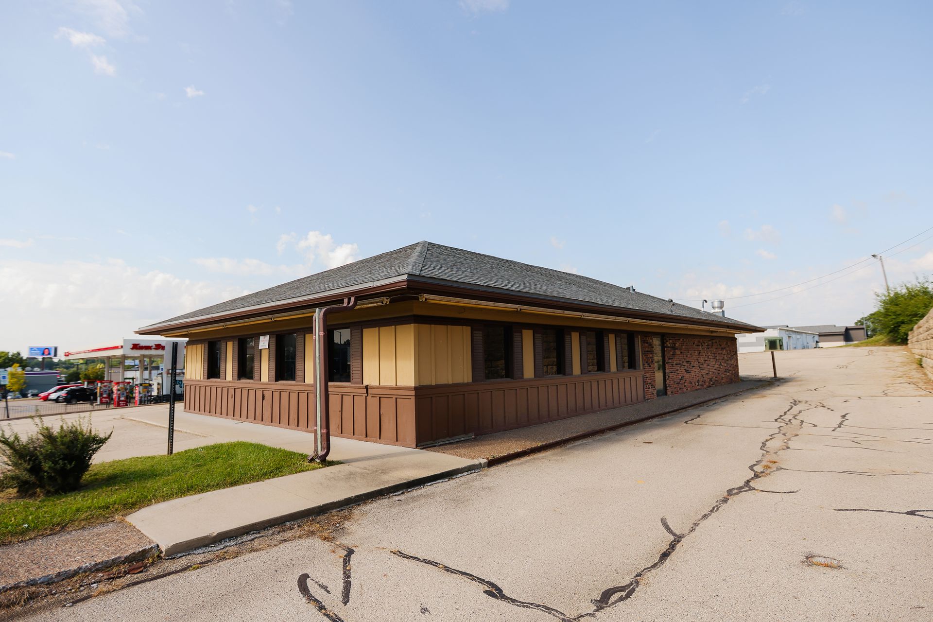 A small brown building with a gray roof is sitting on the side of a road.