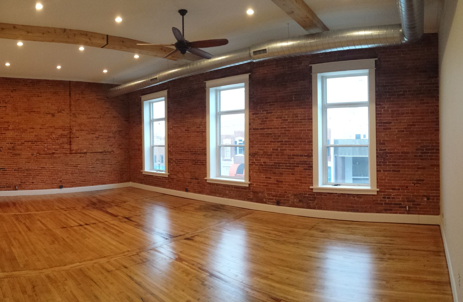 A large empty room with hardwood floors and a ceiling fan.