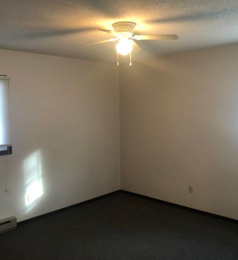 An empty room with a ceiling fan and a window.