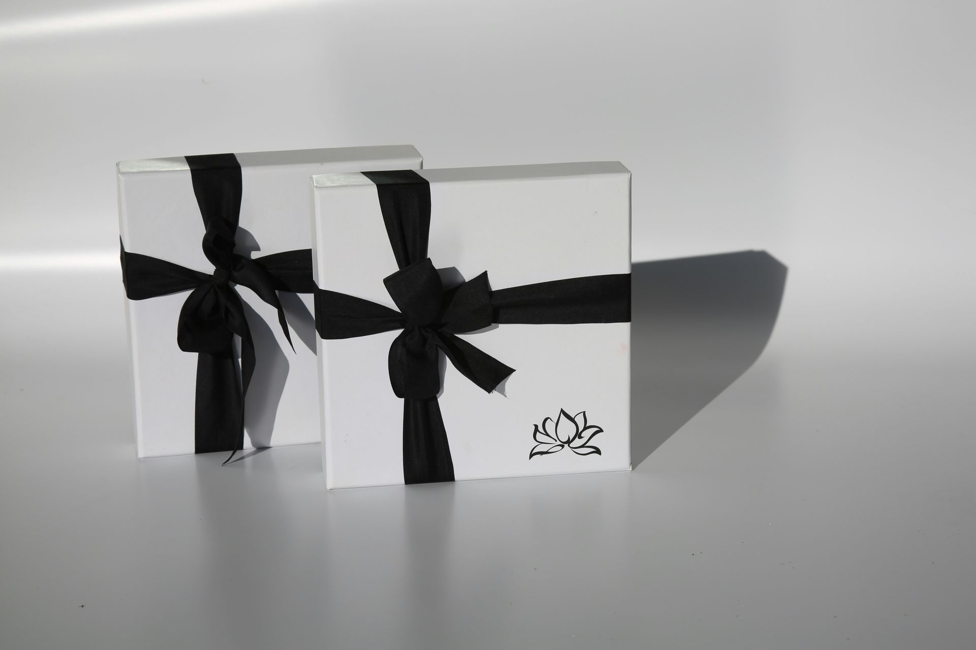 Two white gift boxes with black ribbons. A logo on the bottom-right box.