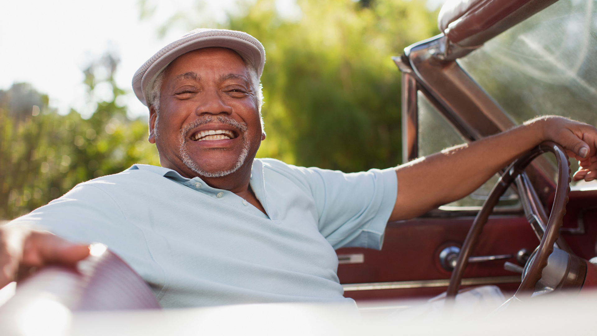 Smiling man in a light blue shirt and cap relaxing in a vintage car outdoors