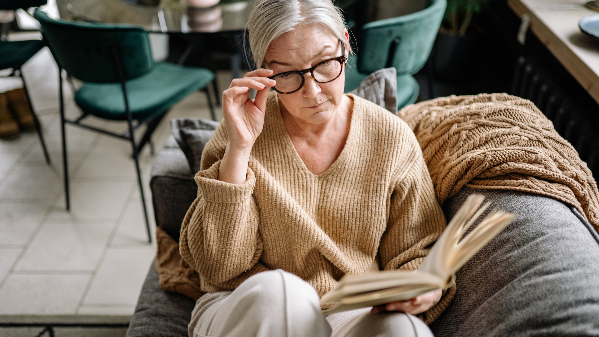 Woman in a cozy sweater reading a book on a sofa in a modern café