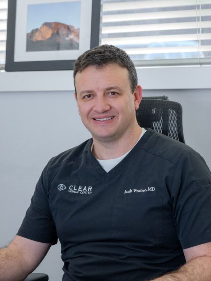 Man smiling in a black polo shirt seated in an office with framed wall art behind him