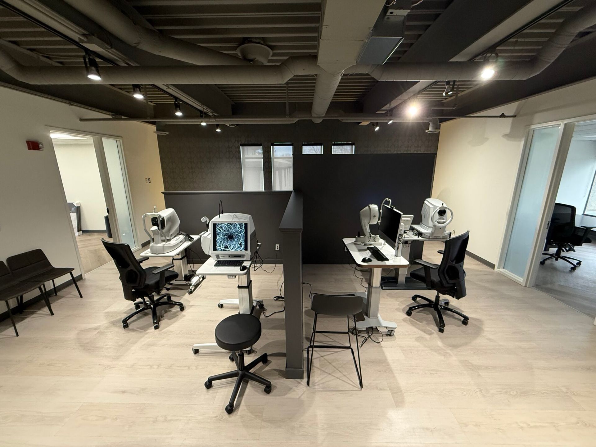 Open office with desks, office chairs, desktop computers, and light wood flooring under exposed ceiling beams.