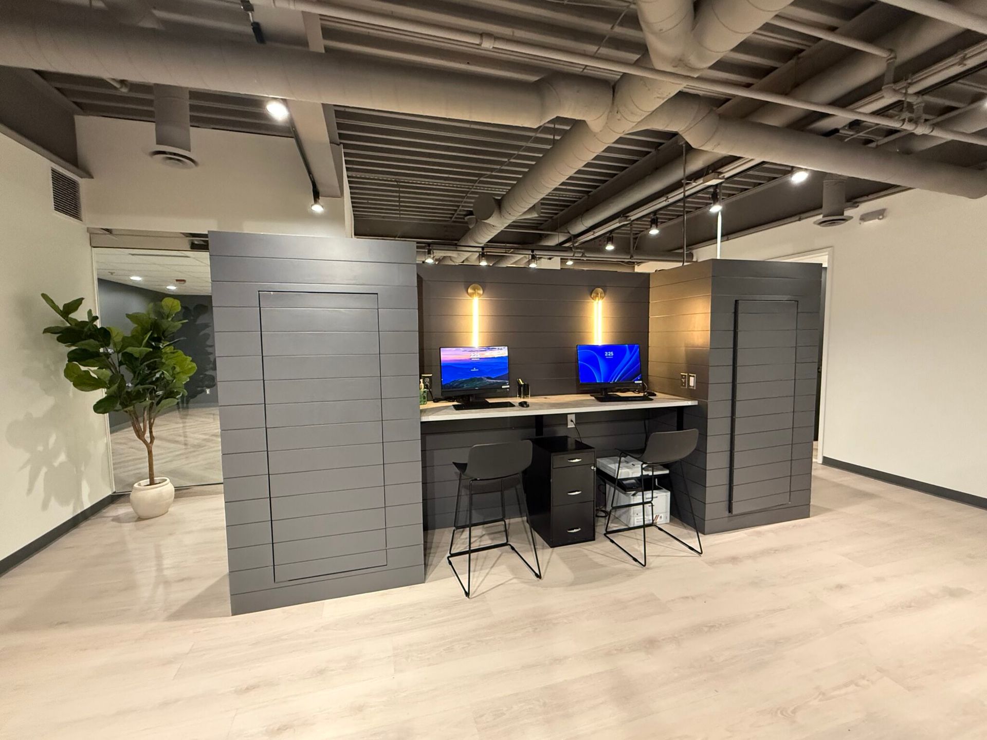 Modern office workspace with two desktop monitors, desks, chairs, and tall gray partitions