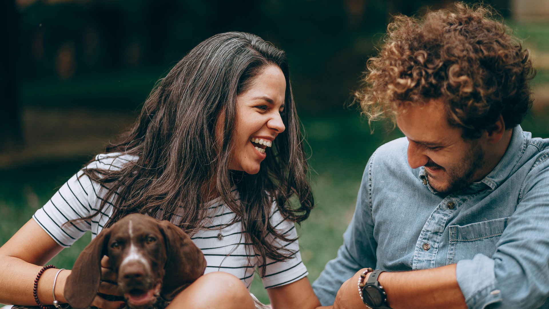 Two people smiling outdoors with a brown dog on a leash
