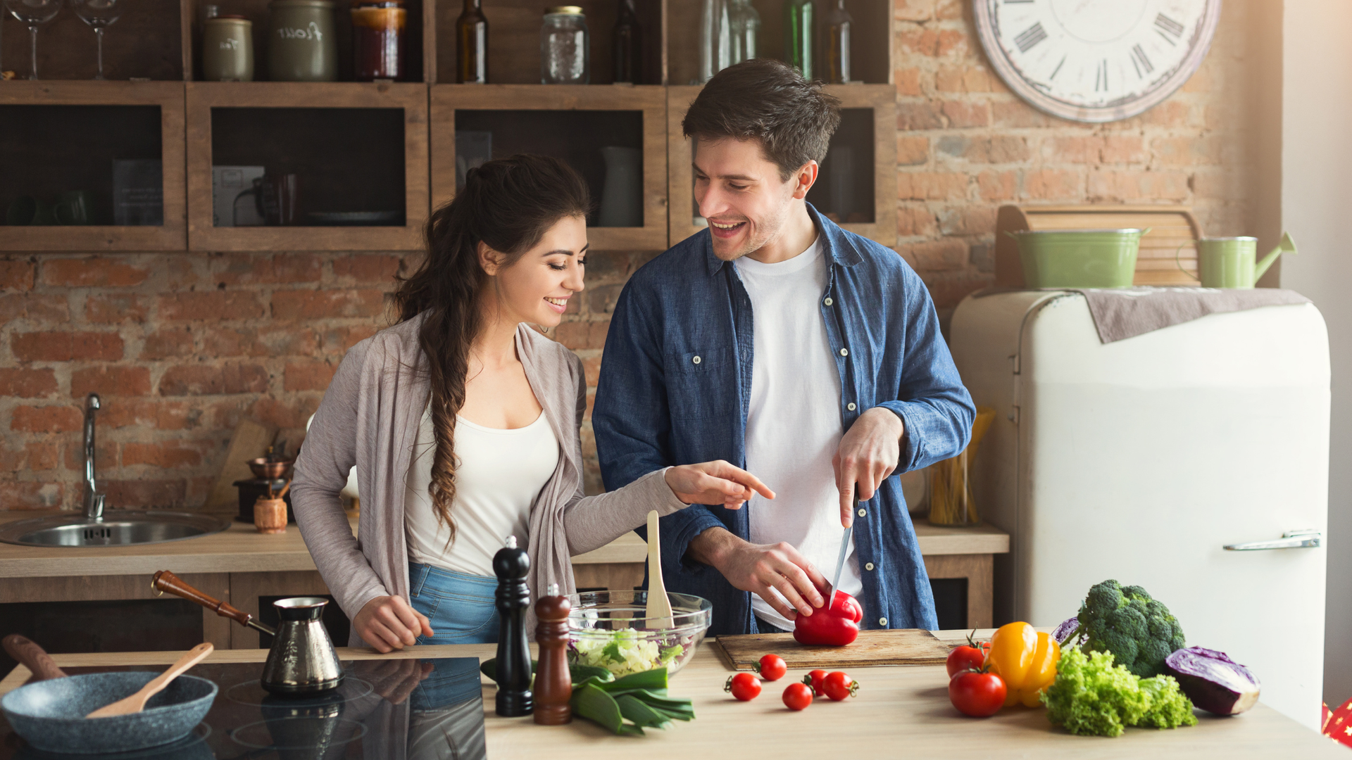 Two people preparing food in a modern kitchen, one pouring ingredients into a mixer while holding a cabbage