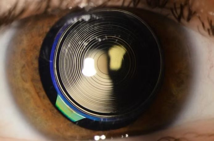 Woman smiling, blue sky background, wearing denim shirt and white tee.