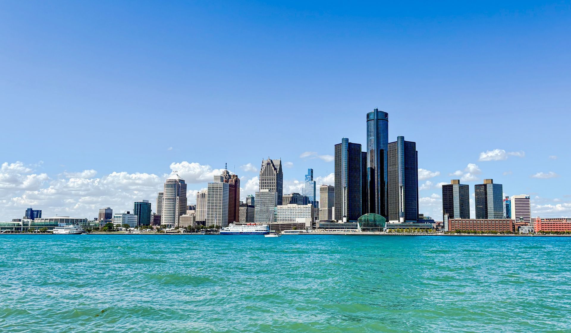 City skyline across turquoise water under a blue sky, with tall modern buildings and waterfront structures.