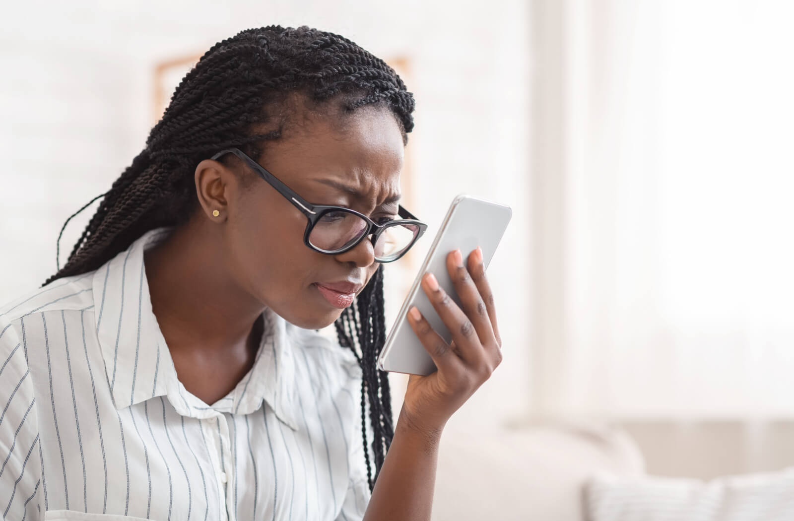 Woman in glasses looking at a smartphone with a puzzled expression in a bright room