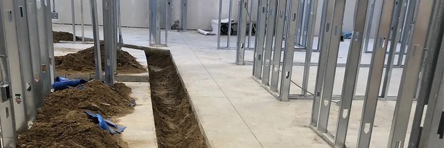 Construction site hallway with metal framing, concrete floor, and a narrow trench along the left side