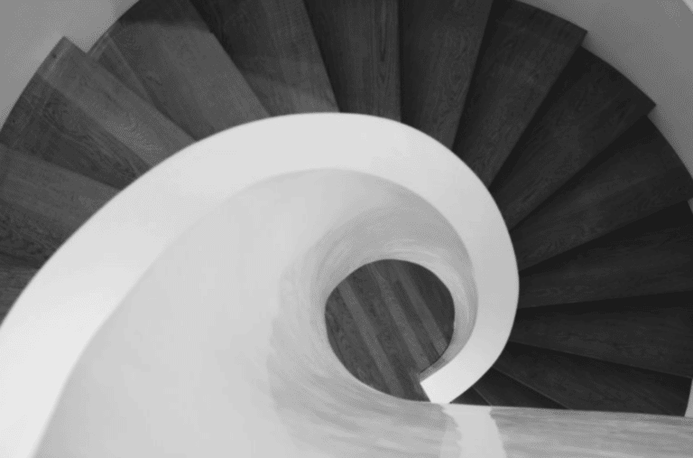 Black-and-white spiral staircase viewed from above, with a curved white railing and dark steps