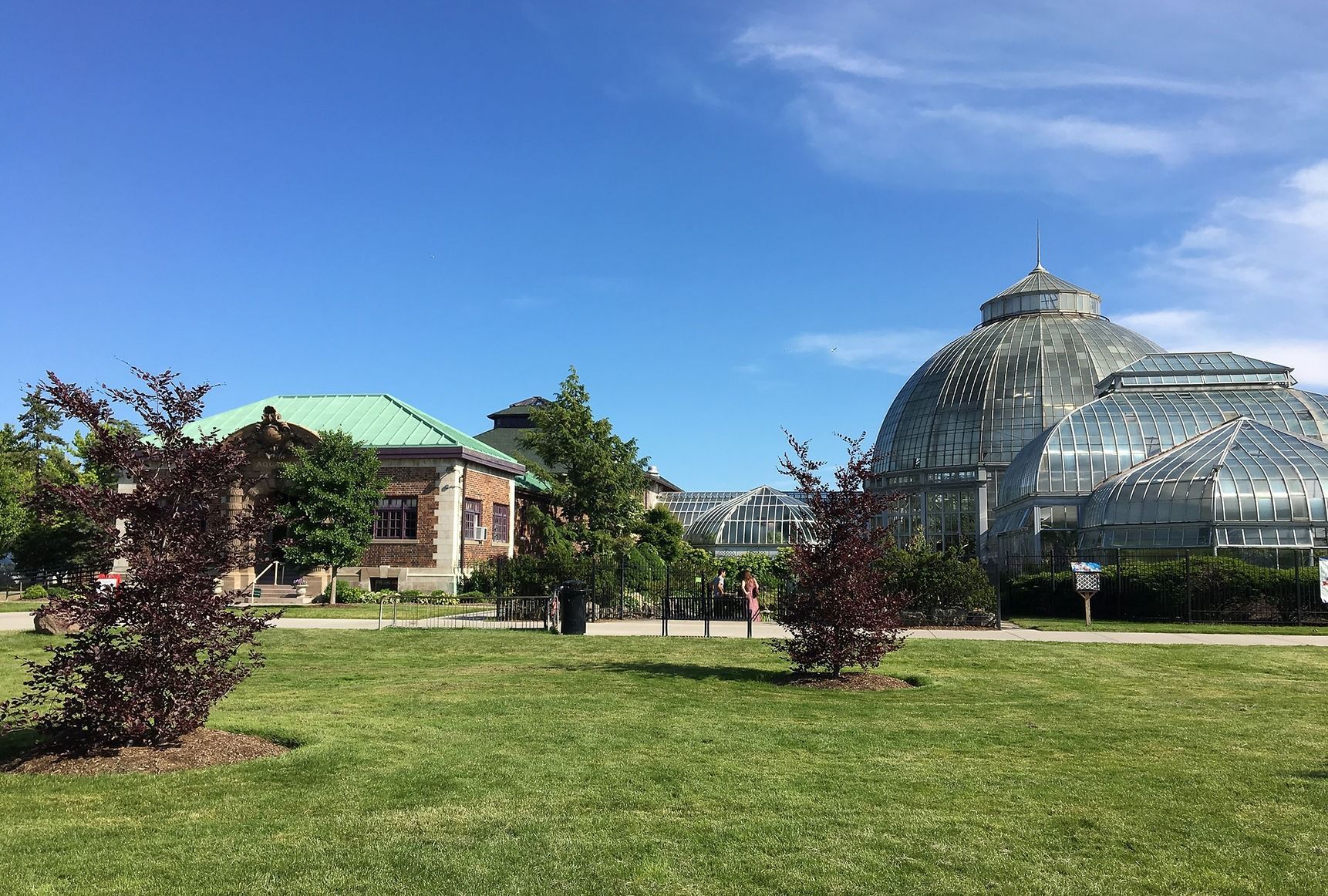 Botanical garden with a glass-domed conservatory, a small building, and green lawn under a blue sky