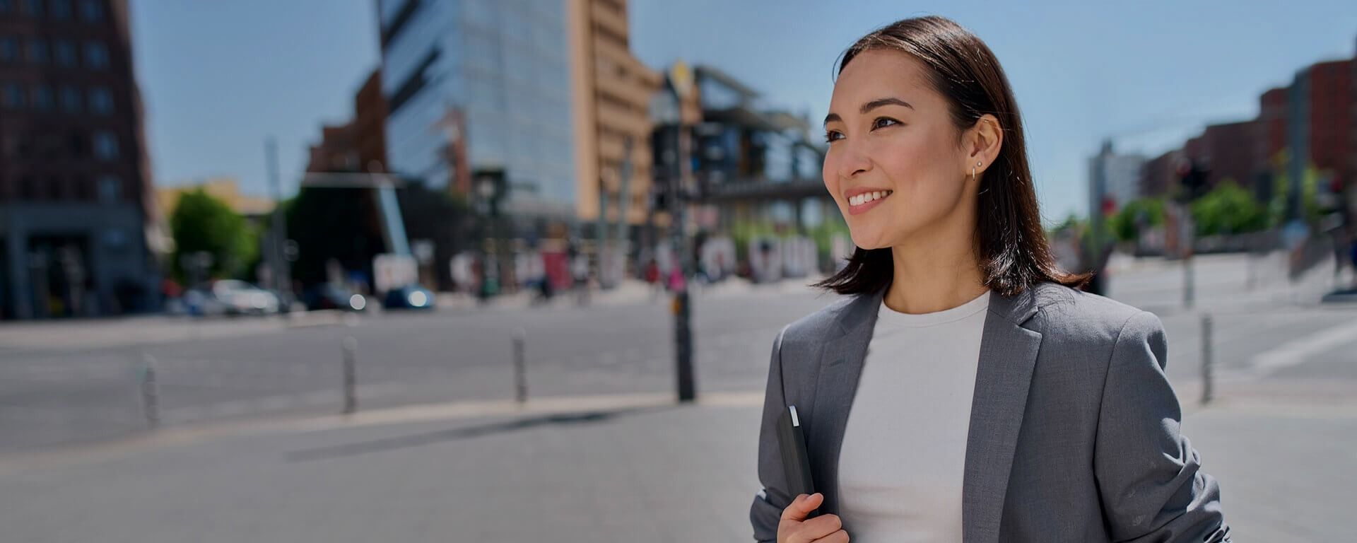Smiling woman in a gray blazer standing outdoors on a city street in daylight