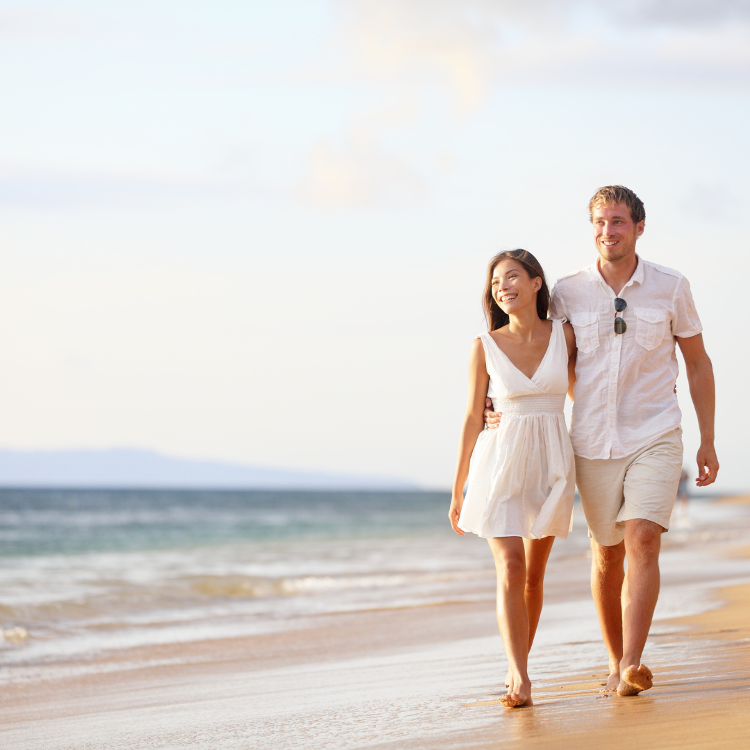 Couple walking hand in hand along a sunny beach with ocean waves in the background