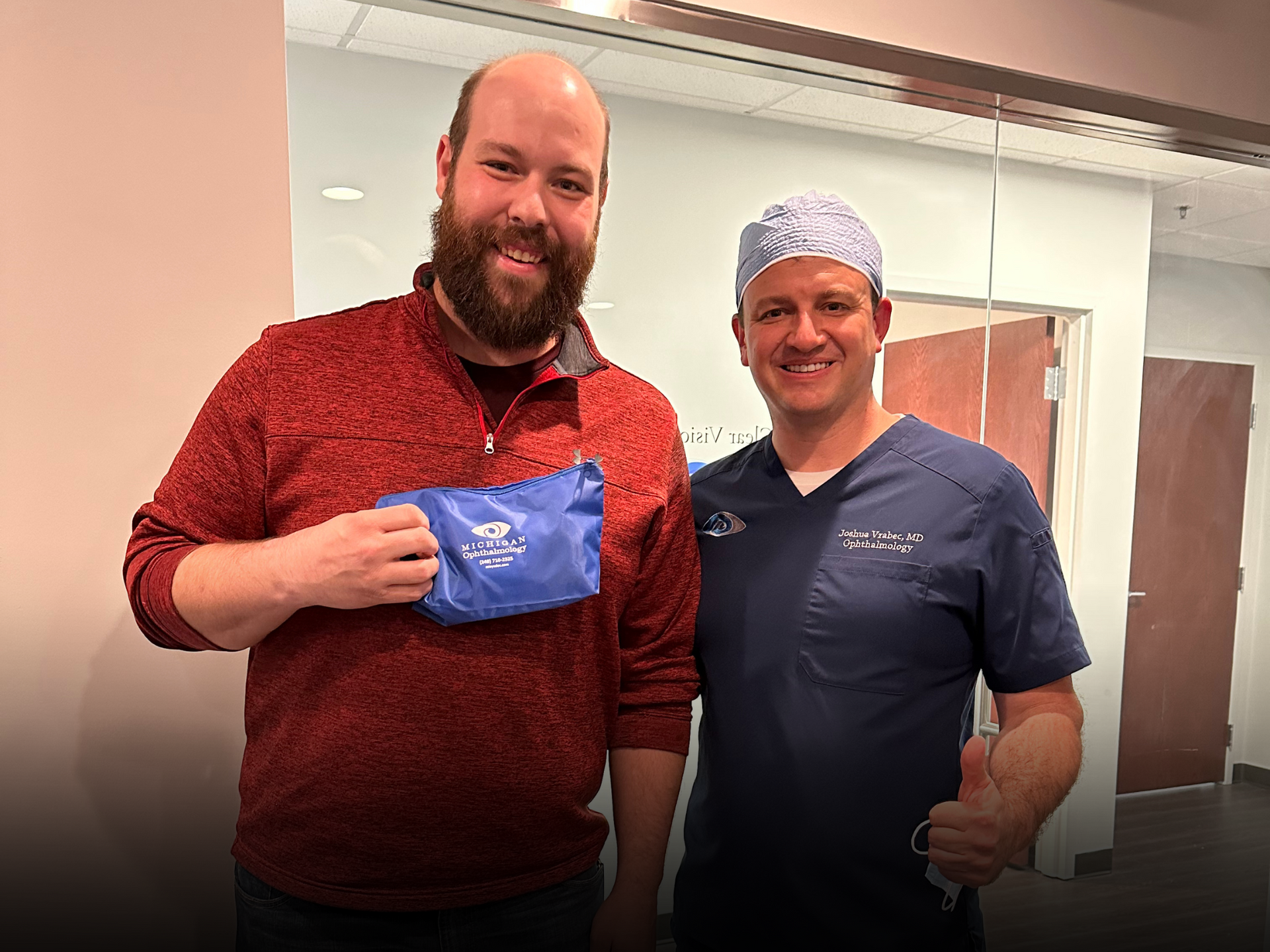 Two smiling people in scrubs, one holding a blue gift bag, standing in a hallway.