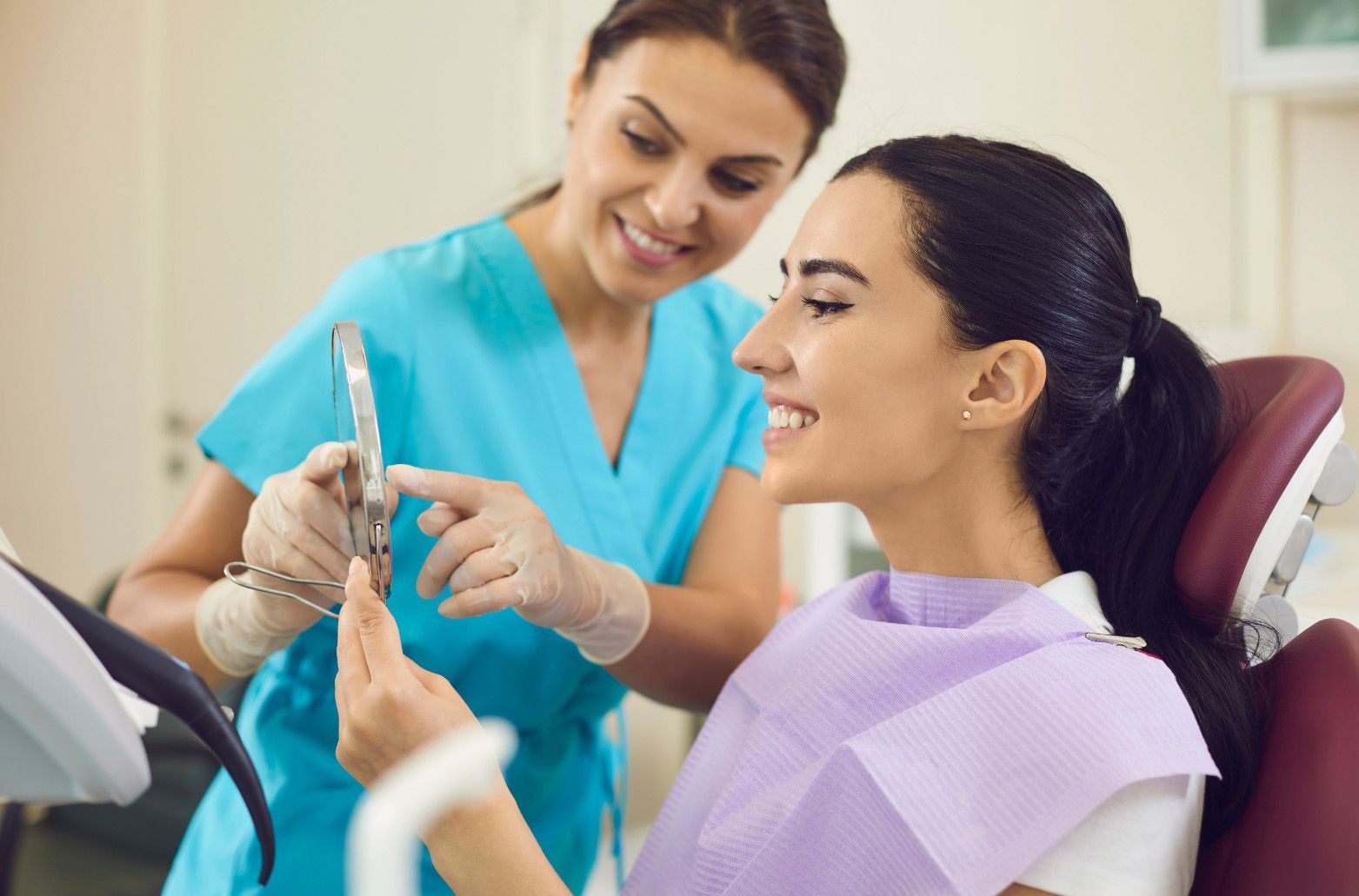 Dentist with mask and gloves examining a female patient's teeth in a dental office.