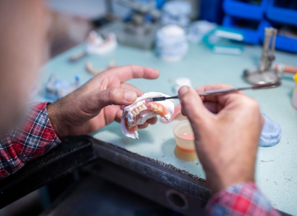 Person working on a dental mold with tools in a lab setting, focused on the details.