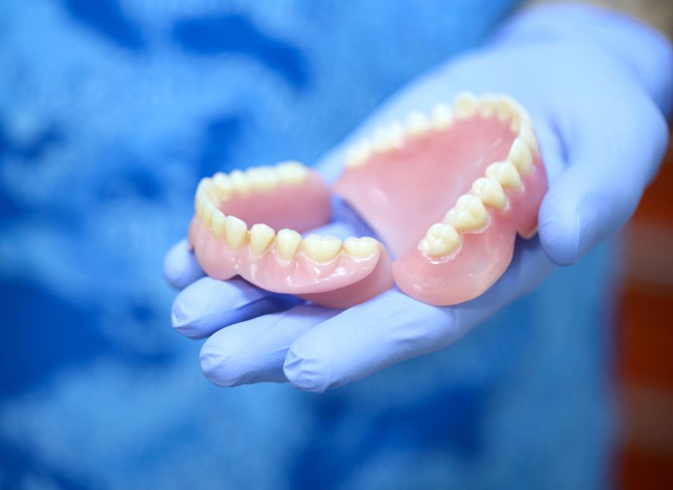 Man smiling, holding new dentures, doctor pointing. Dental office setting.