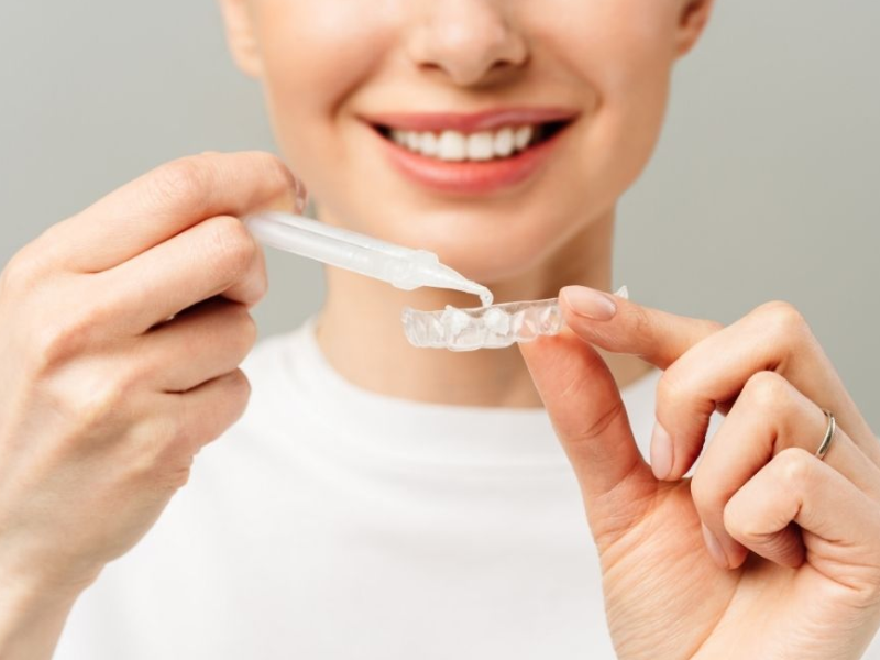 Woman smiling, pointing to a dental model showing a tooth implant, blue background.