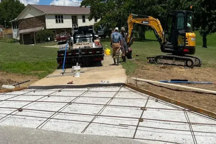 Construction site: Concrete driveway with rebar grid, small excavator, and workers in a residential area.