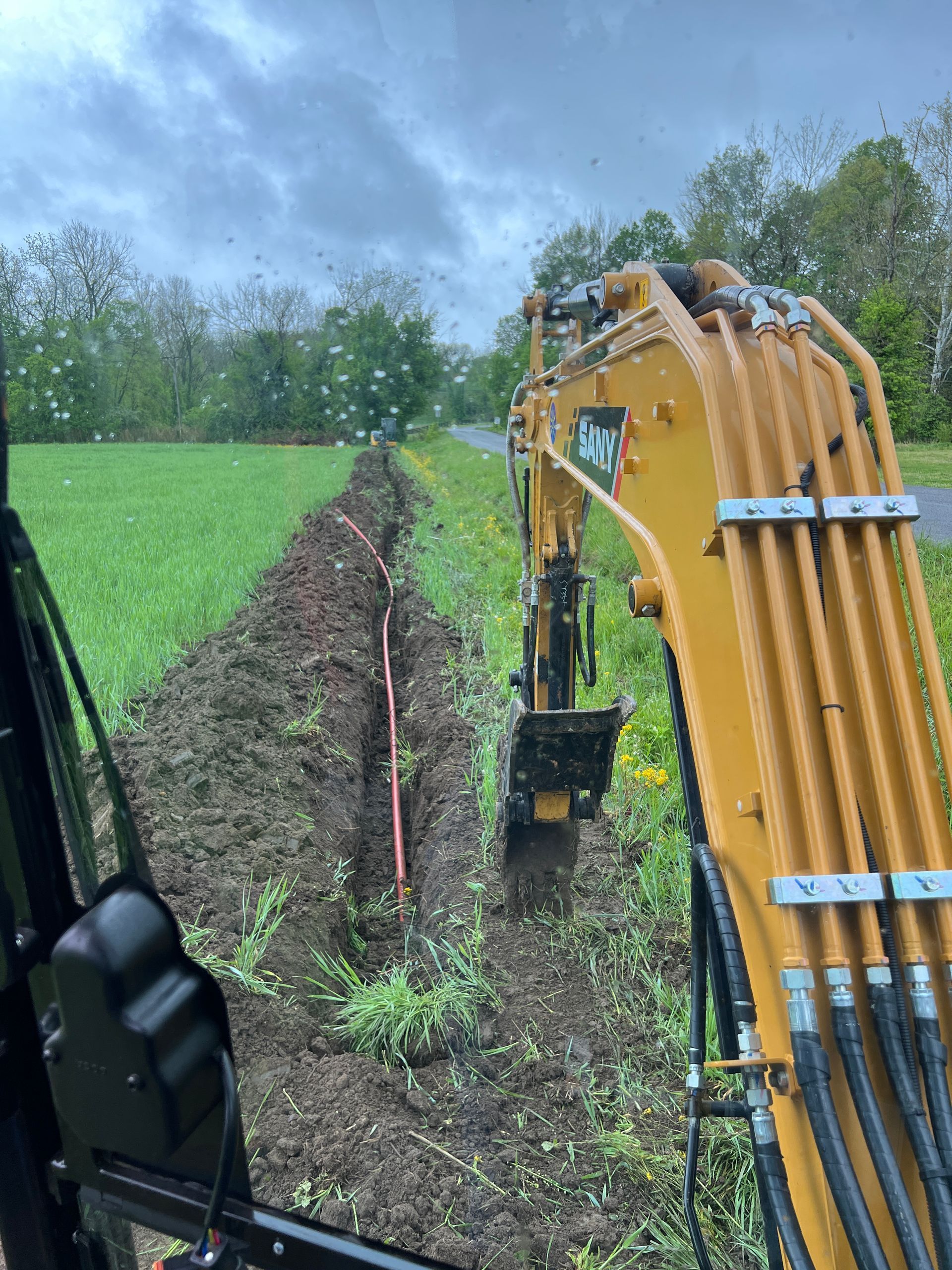 a yellow excavator is digging a trench in a field .