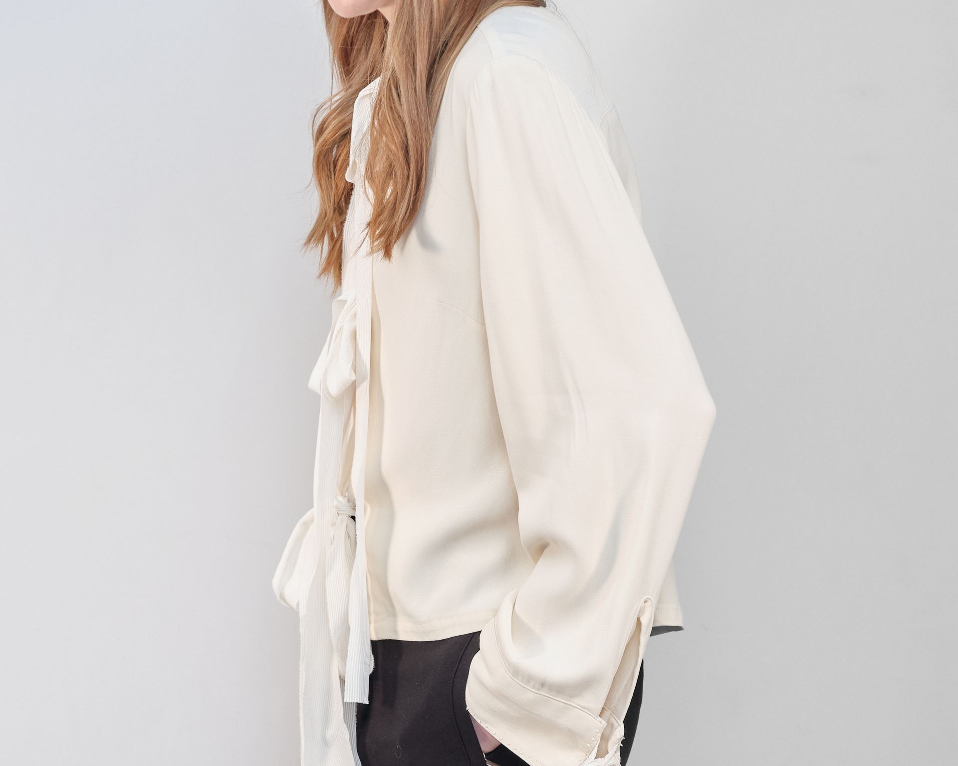 A woman is wearing a white shirt with a bow and black pants.