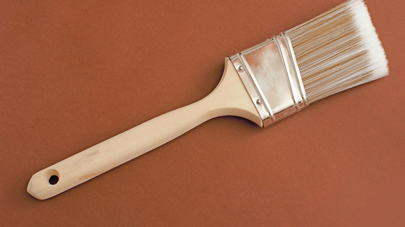 Paintbrush with wooden handle, white bristles, and silver metal band on a brown background.