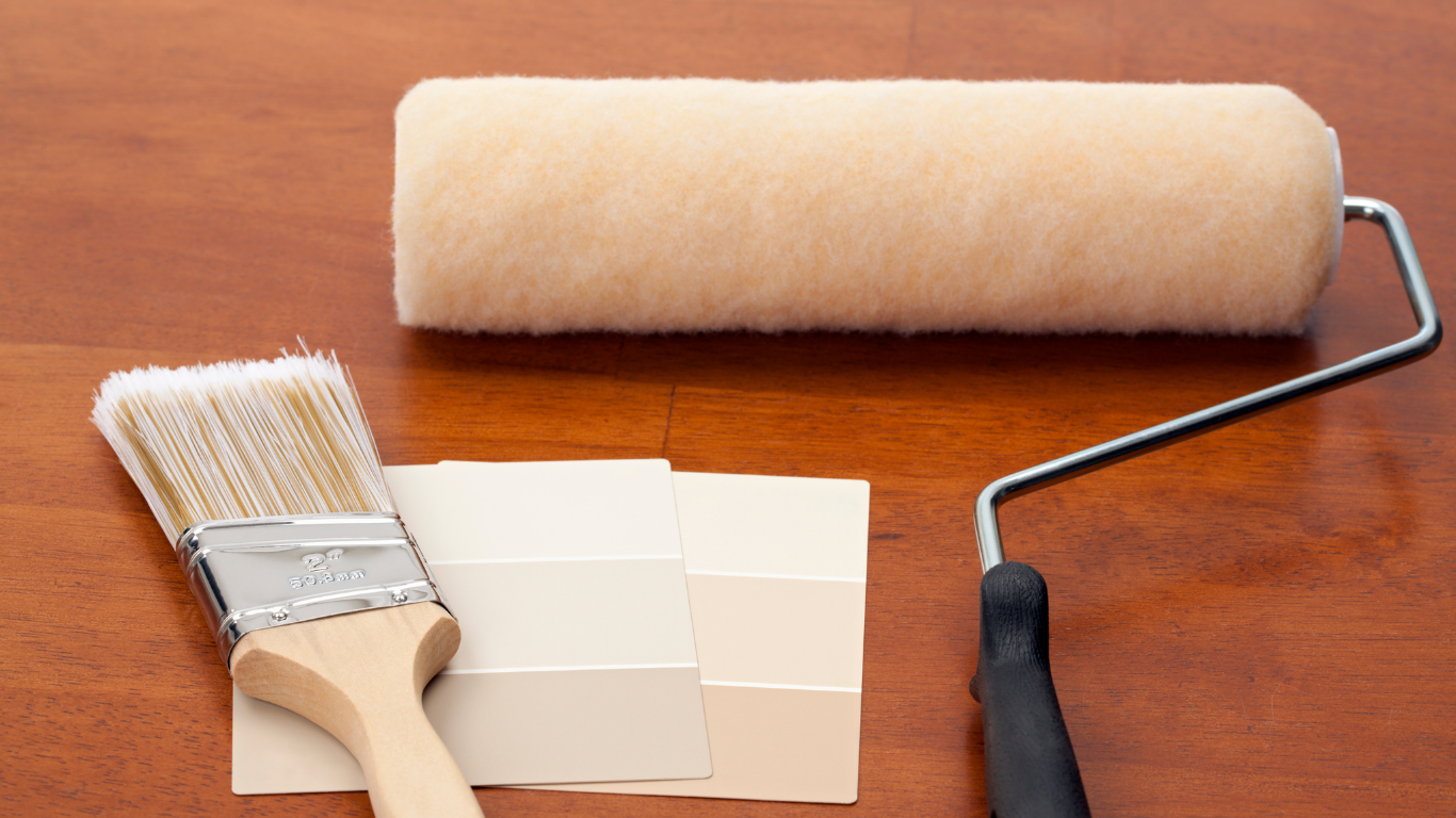 Paint roller, brush, and paint swatches on a wooden surface, ready for painting.