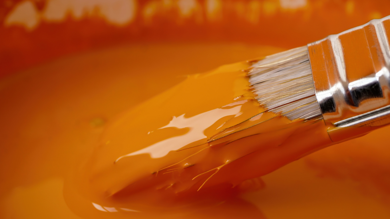 Paintbrush dipped in bright orange paint.