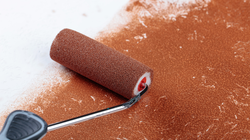 Paint roller applying copper-colored paint to a white surface.