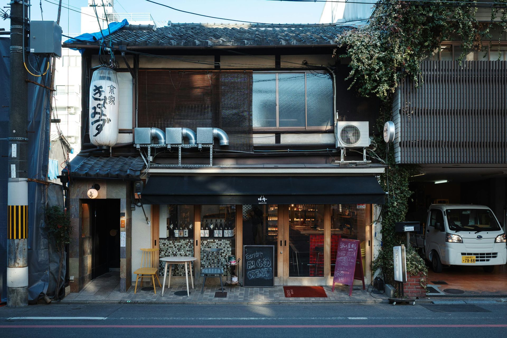 Japanese shop with a dark awning, a hanging lantern, and a small white car parked nearby.