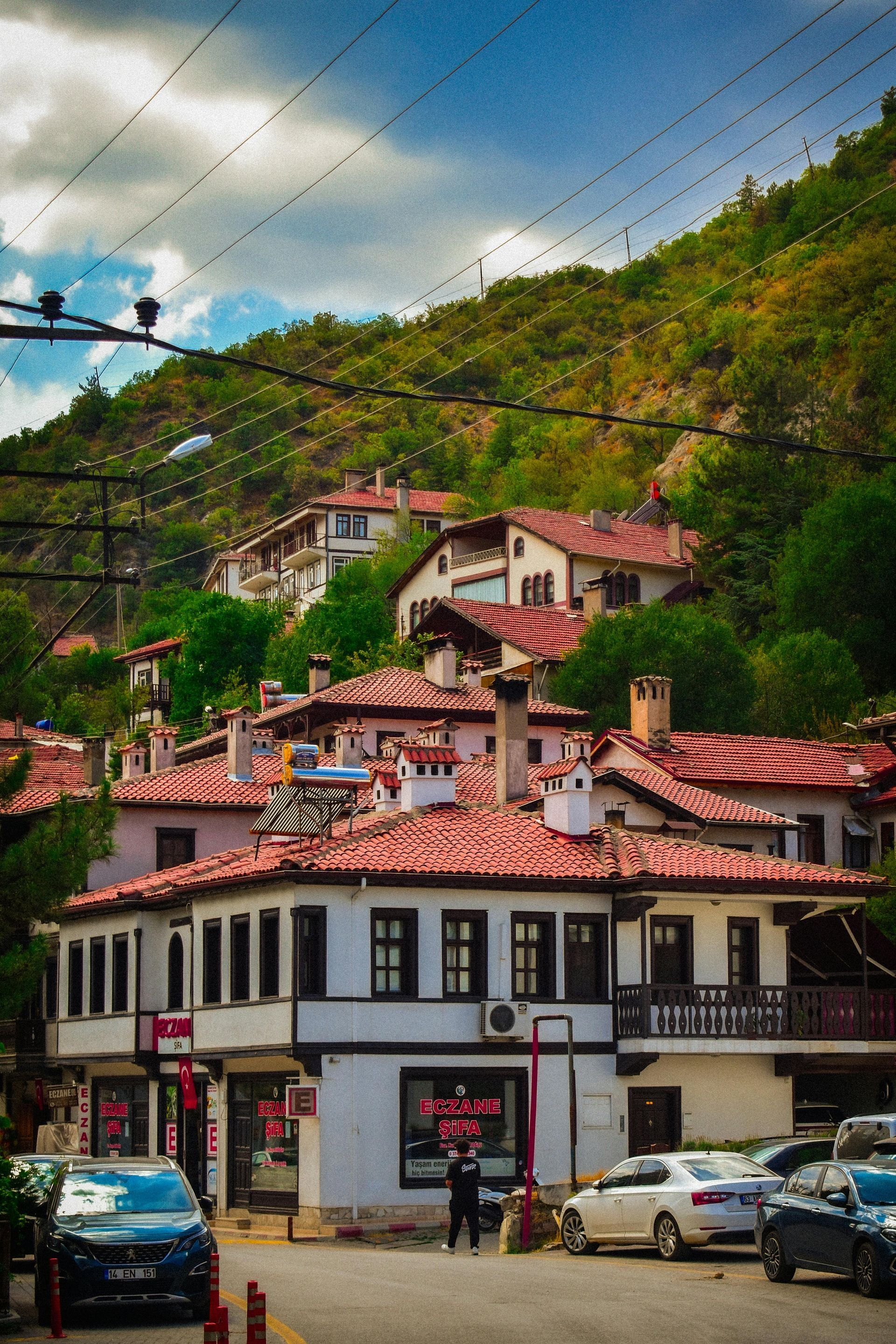 White houses with red tile roofs nestled on a green hillside; cars parked in front.
