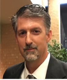 A woman wearing a black polo shirt is standing in front of a wall.