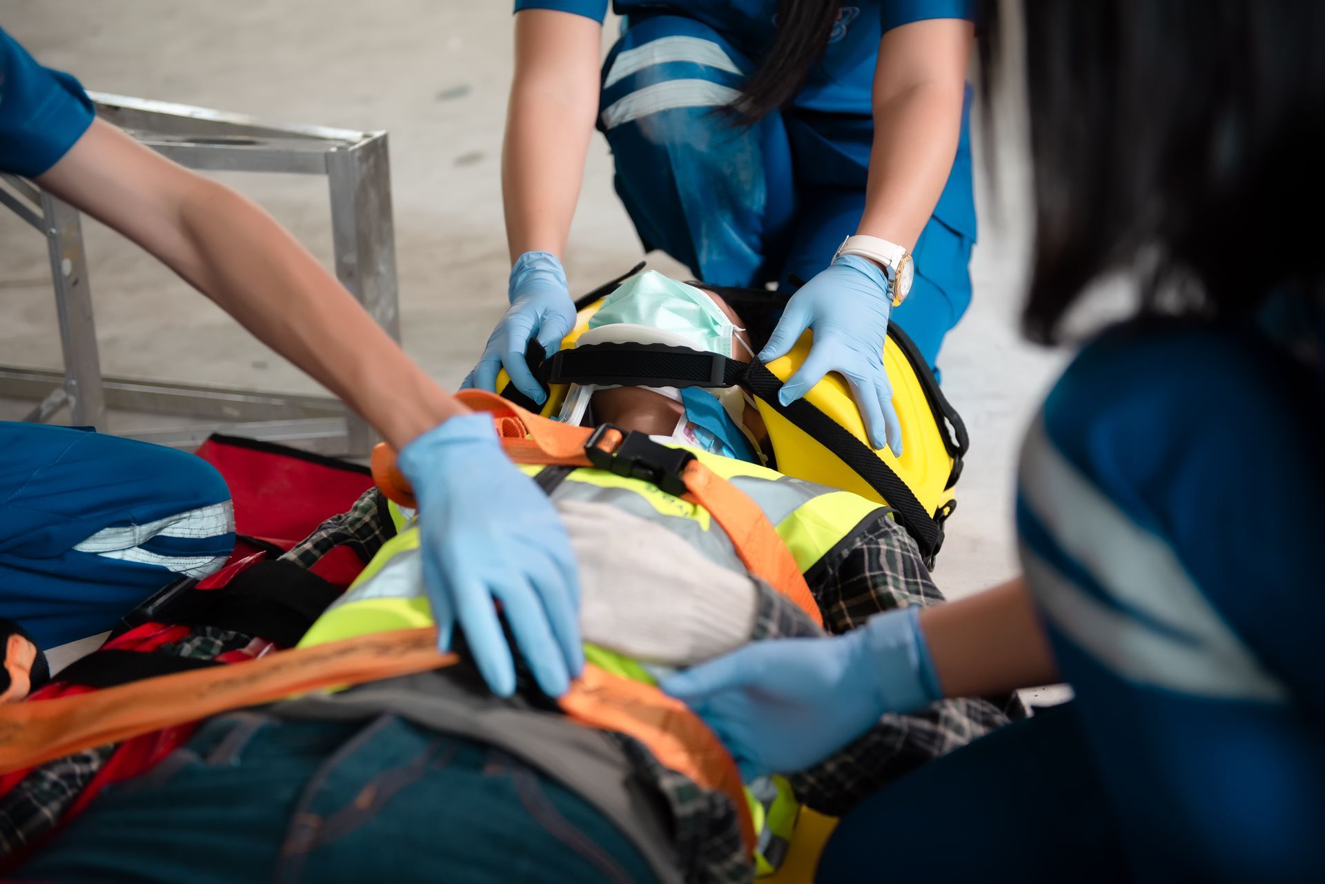 Medical personnel securing a person on a stretcher. The person wears a neck brace and blue-gloved hands are visible.