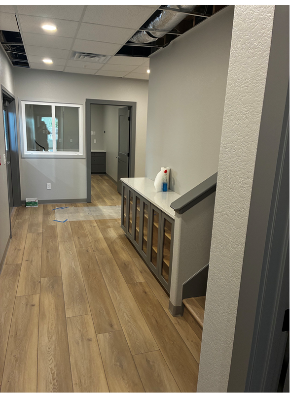A hallway with light wood floors, gray walls, a built-in cabinet with a white top, and unfinished ceiling panels.