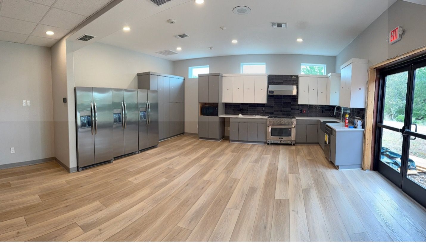 A modern kitchen featuring stainless steel refrigerators, grey cabinets, a stove, and light wood flooring.