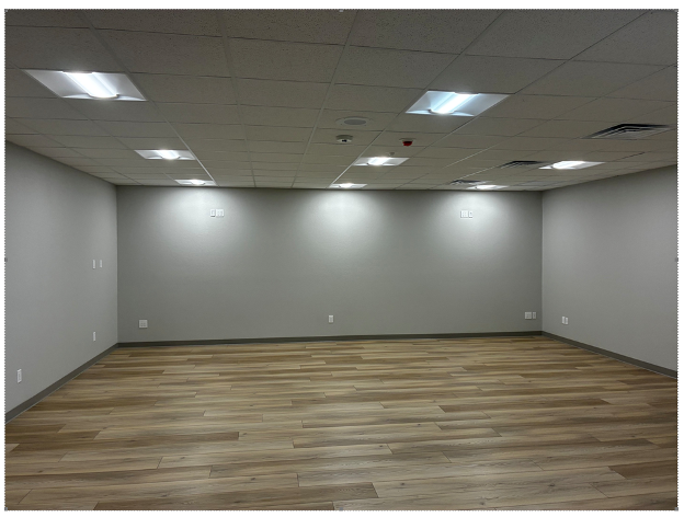 An empty room with light grey walls, light wood-look flooring, and a drop ceiling with recessed rectangular light panels.
