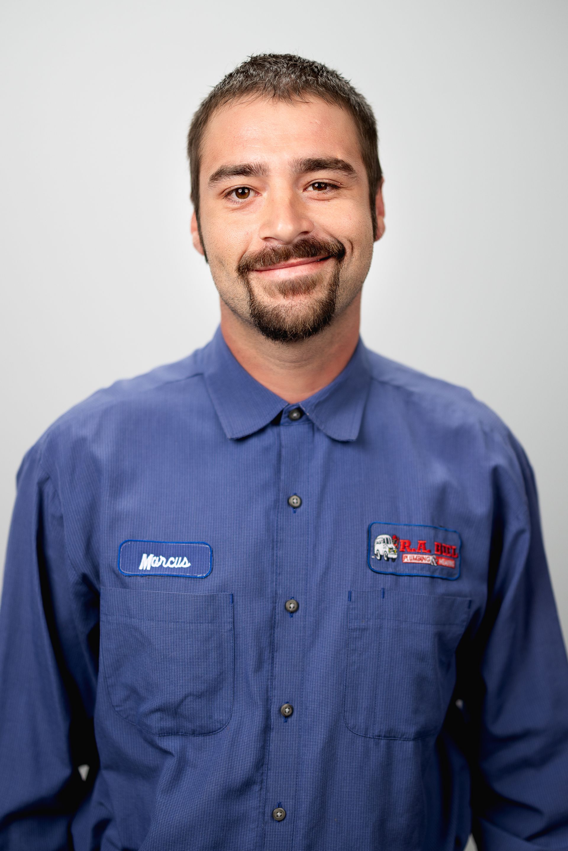 A man with a beard is wearing a blue shirt and smiling for the camera.