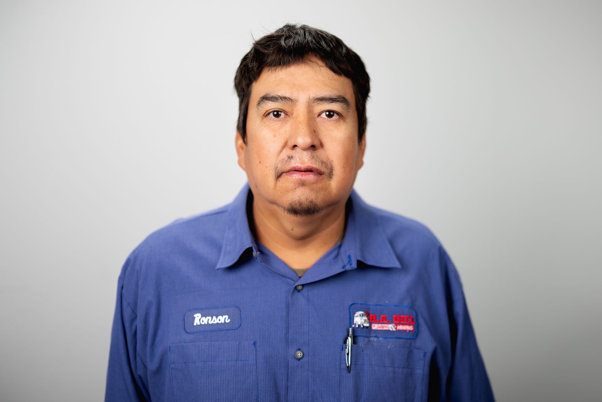 A man in a blue shirt is standing in front of a white background.