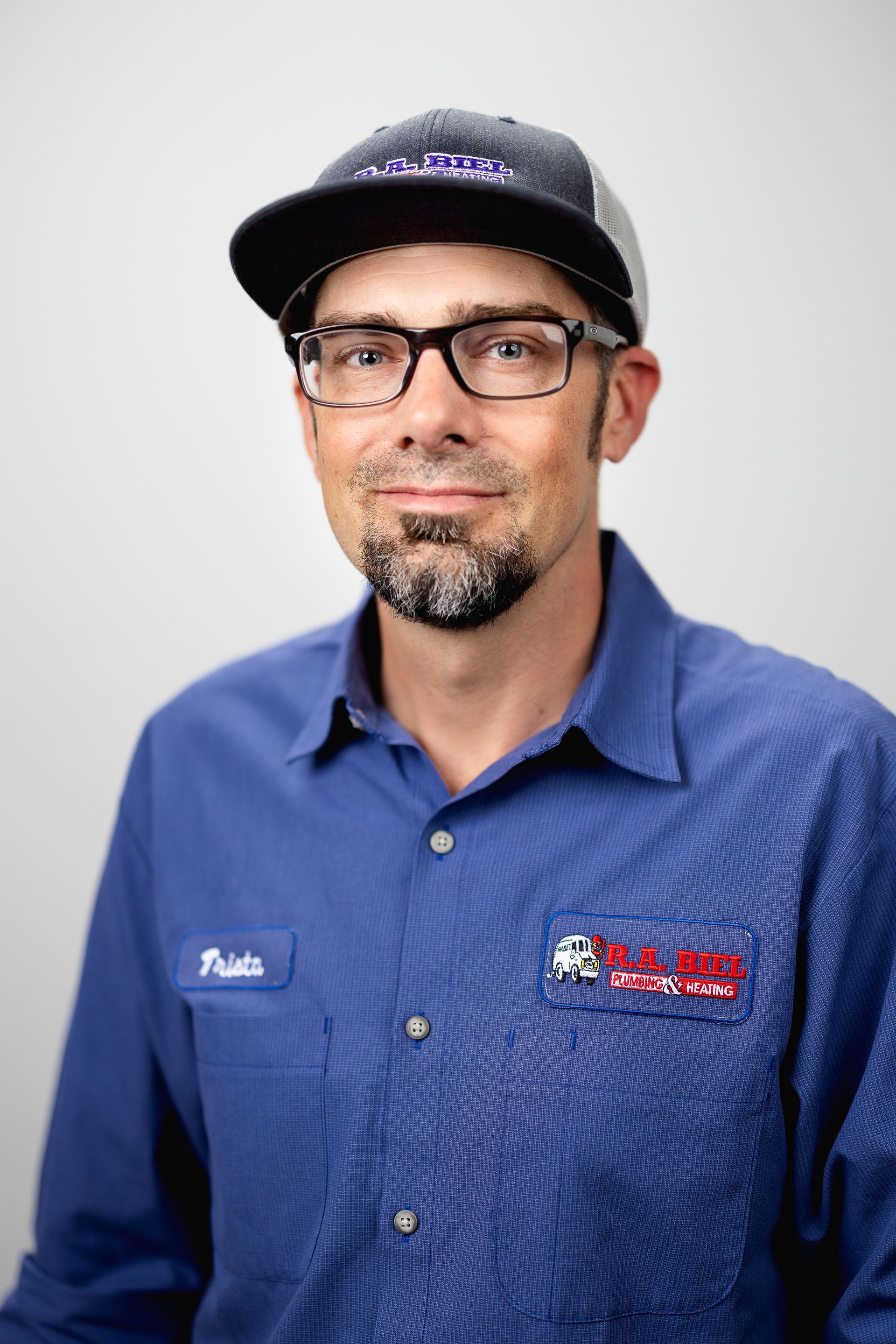 A man wearing glasses and a hat is standing in front of a white wall.