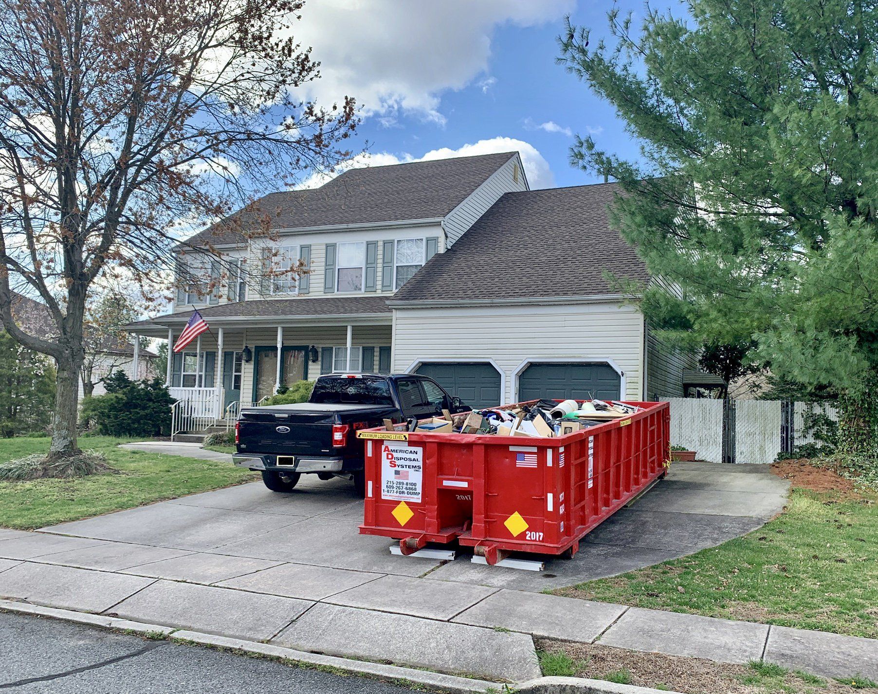 A red, twenty cubic yard dumpster is parked on in front of a house in the driveway